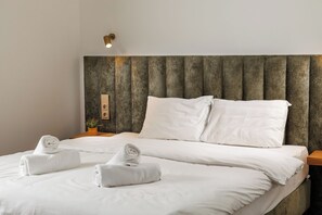 A neatly made bed with white linens and two rolled towels, a wooden headboard, and a small bedside table with a plant. - Richter Residence - Apartment 8 (Brașov)