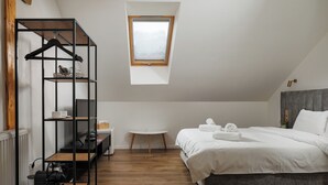 Un dormitorio con cama, una mesita, un perchero y un tragaluz.