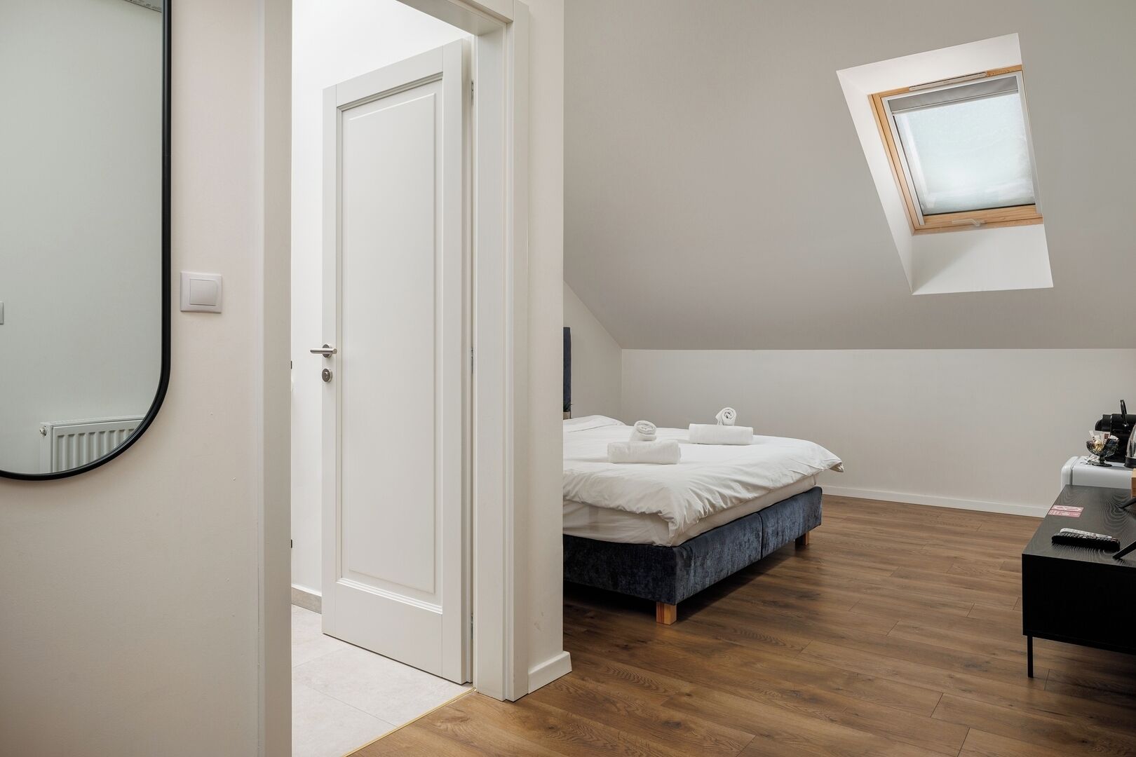 Ein Schlafzimmer mit Bett, Schreibtisch, Spiegel und einem Dachfenster.