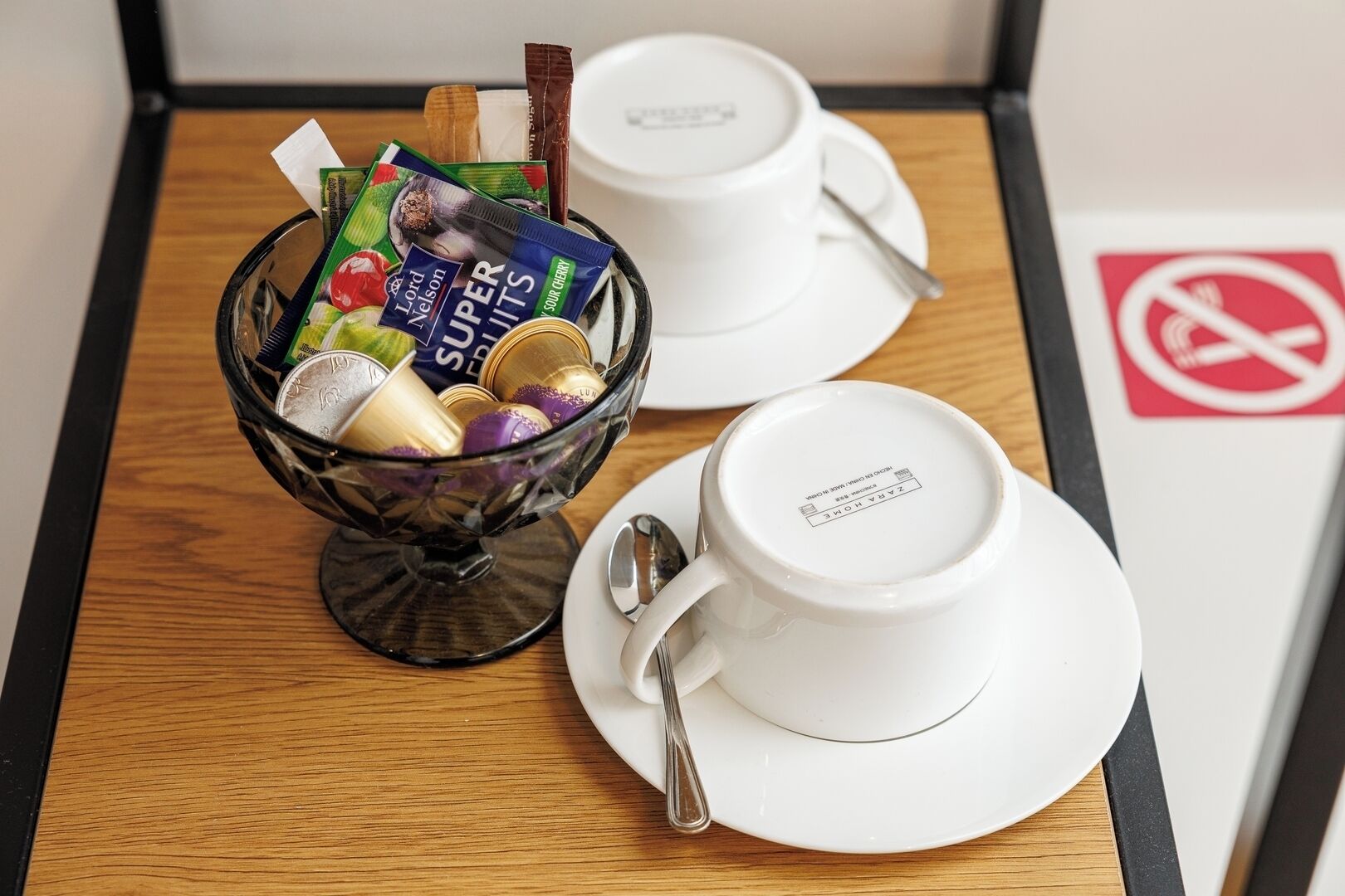 Un plateau de petit-déjeuner avec un bol en verre contenant divers aliments, une tasse blanche et une cuillère, le tout posé sur un plateau en bois.