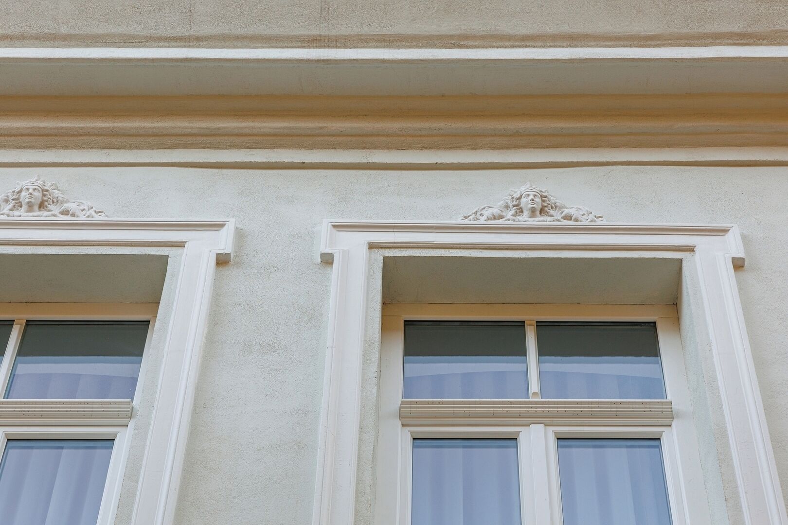 Fachada d'edifici amb dues finestres simètriques, cadascuna emmarcada amb guarnició blanca i rematada amb motllures decoratives.