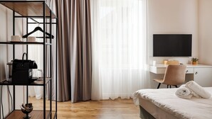 A hotel room with a bed, a desk with a chair, a TV, a wardrobe with a hanger, and a shelf with a handbag and a bowl. - Richter Residence 5 (Brașov)