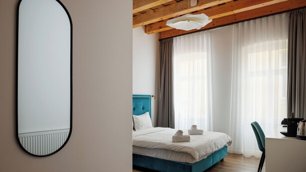 A modern bedroom with a large mirror, a bed with blue headboard, and a desk with a kettle.
