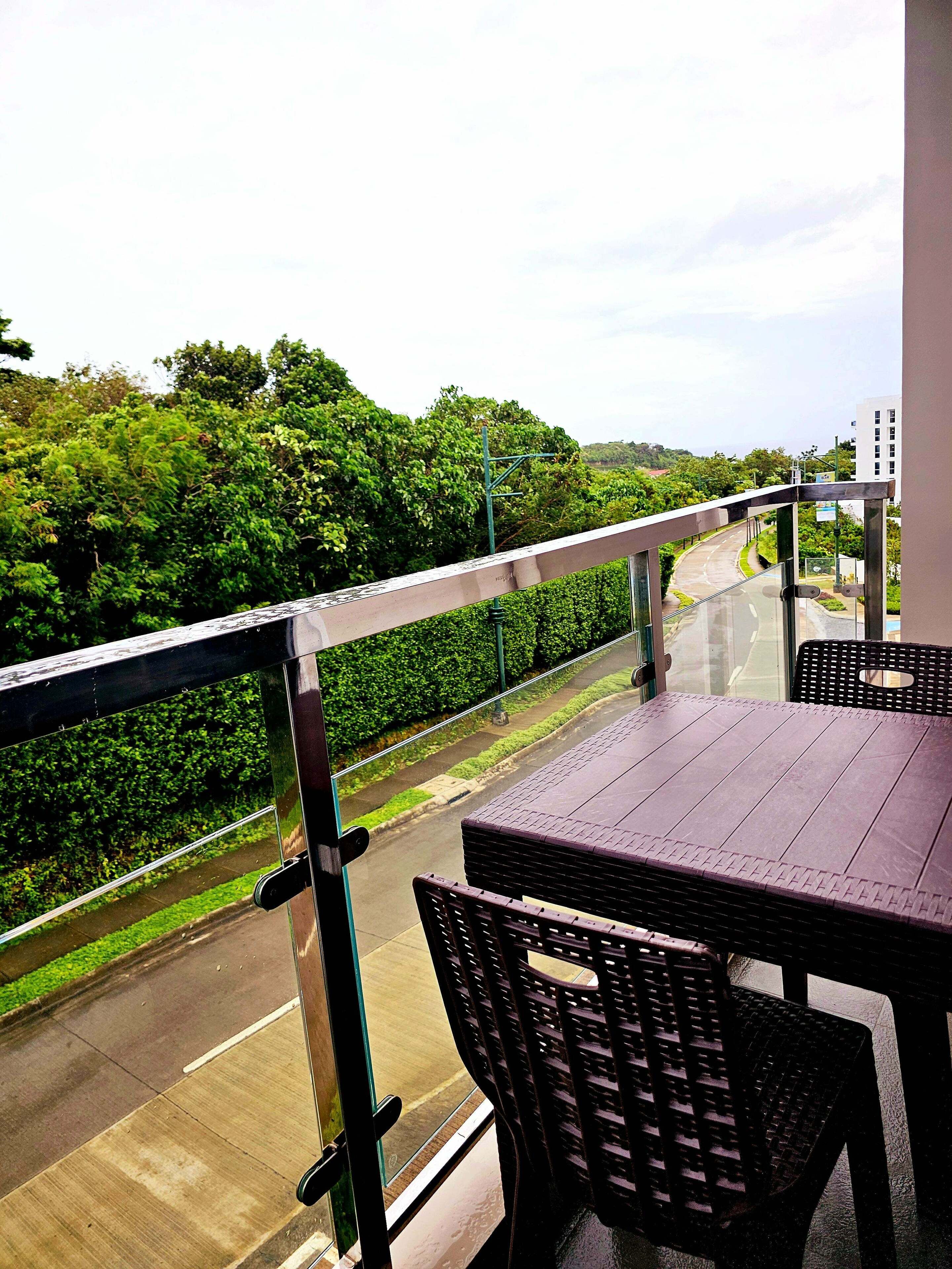 A balcony with a table and chairs, overlooking a road and greenery.