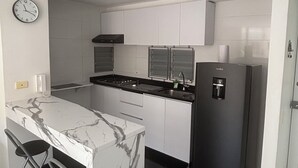 Et moderne køkken med hvide skabe, en marmorø, et sort køleskab og et ur på væggen.