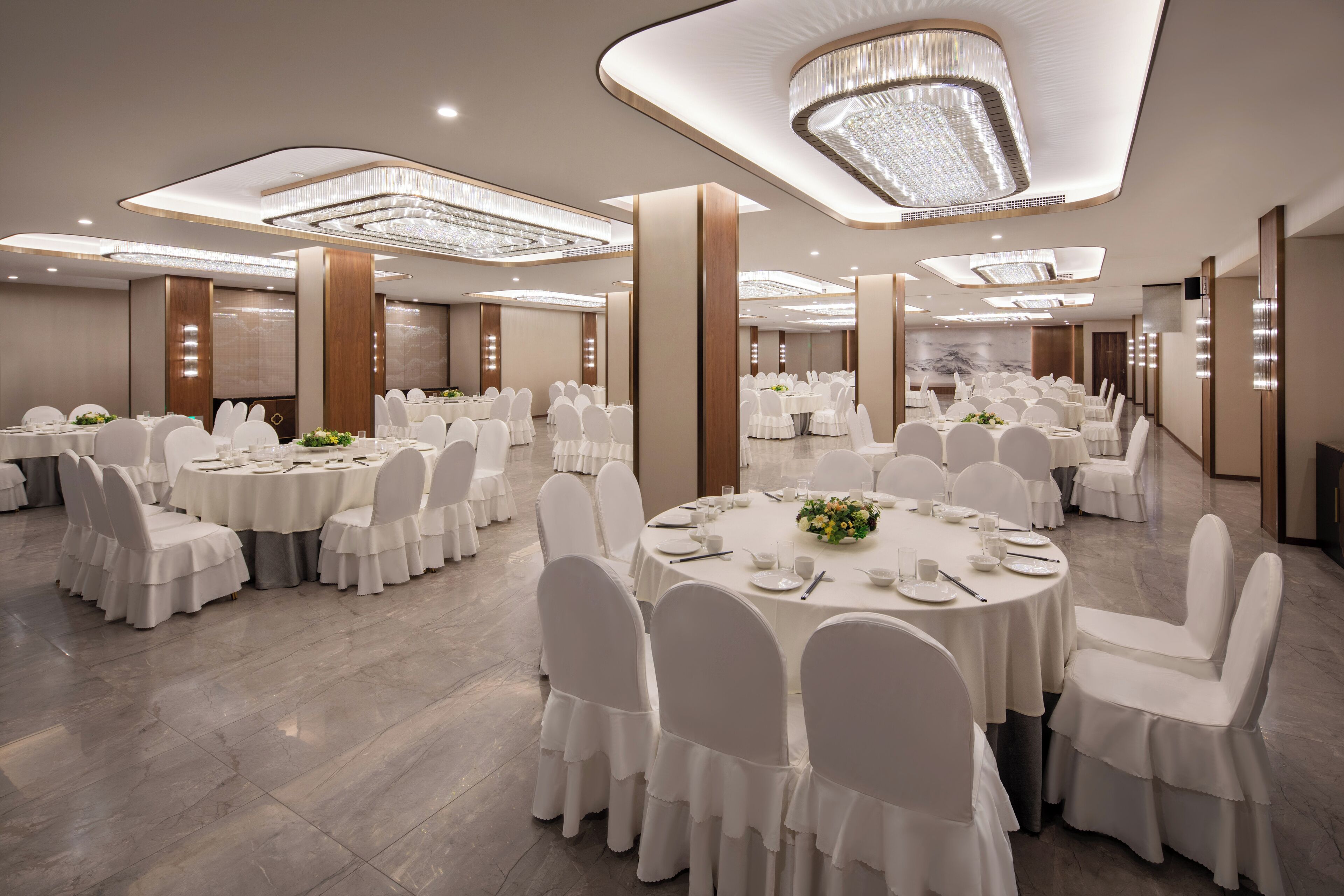 A large banquet hall with round tables, white chairs, and chandeliers.