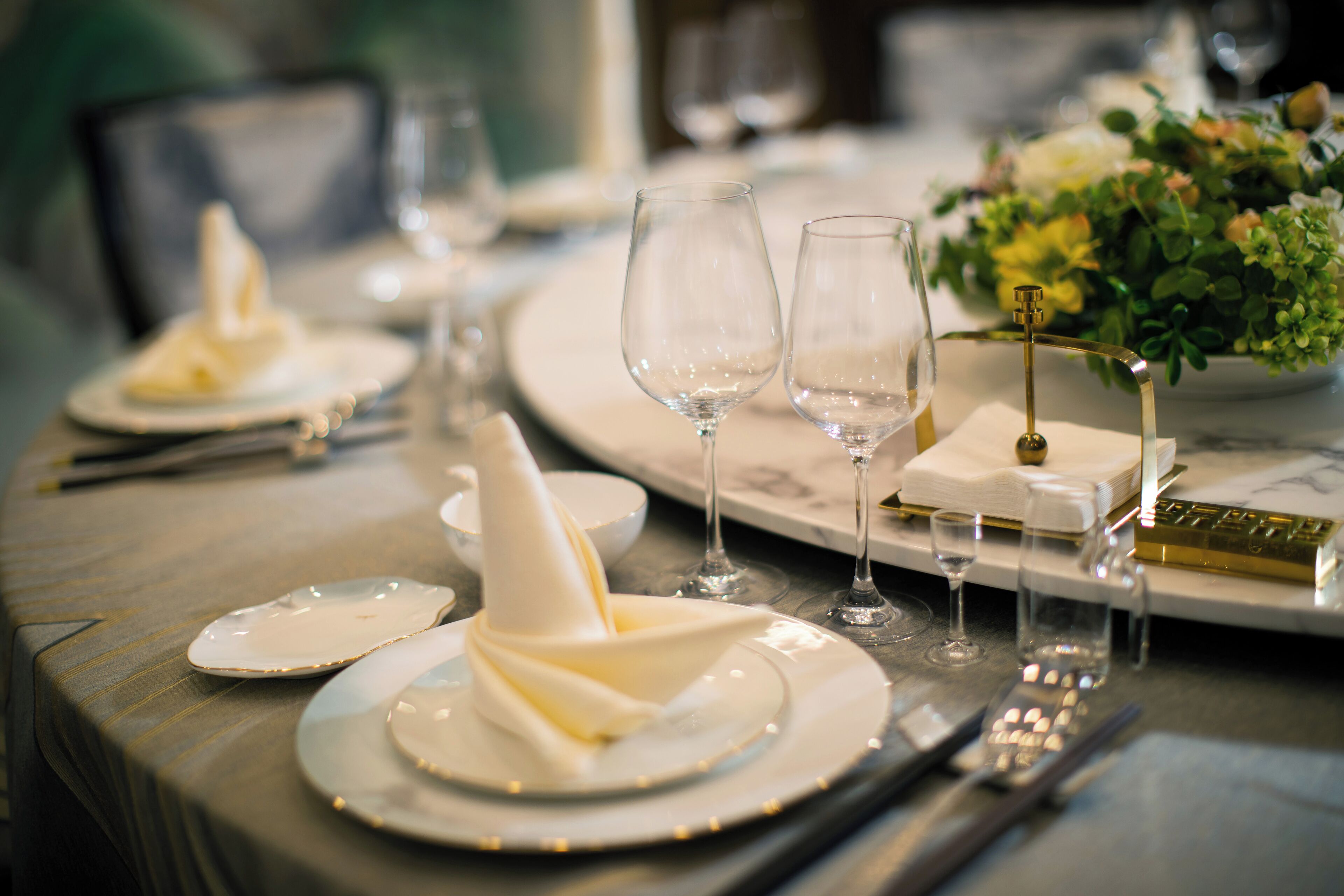 A dining table set with plates, glasses, and cutlery, with a vase of flowers on the right.