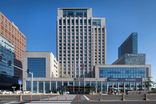A modern hotel with a prominent entrance, multiple floors, and a clear sky. - Beijing Jing Yan Hotel (Beijing)