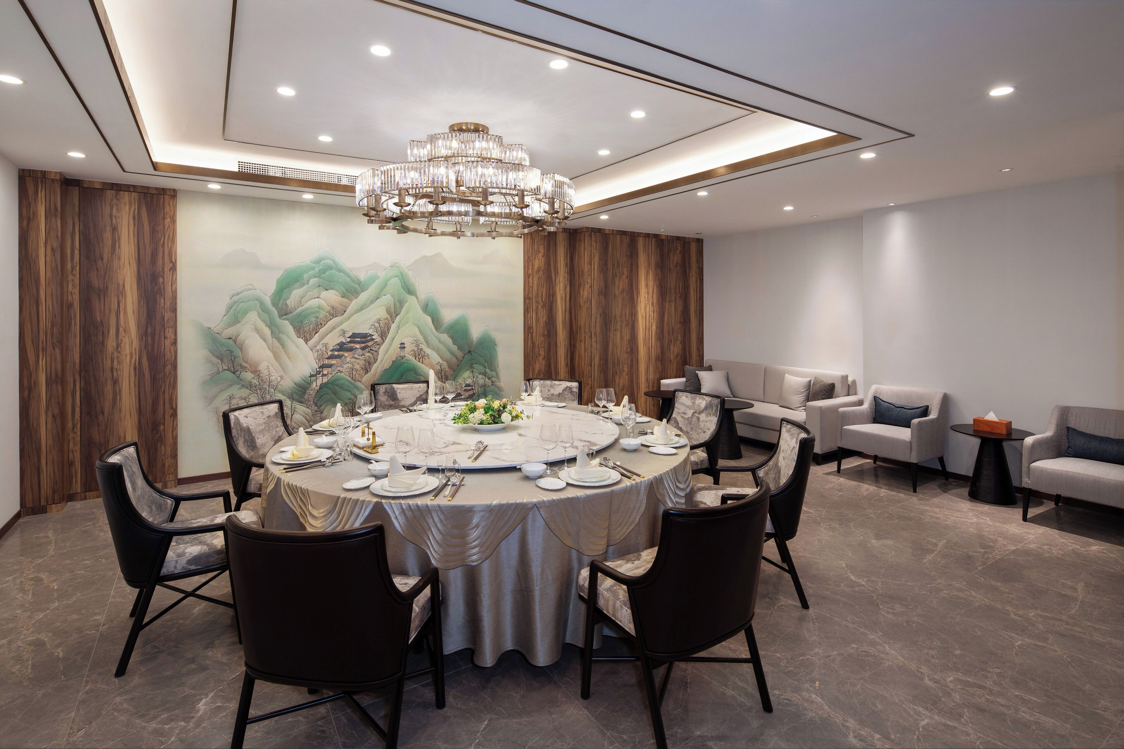 Comedor con una mesa redonda dispuesta para seis comensales, rodeada de sillas, una araña y un mural grande en la pared.