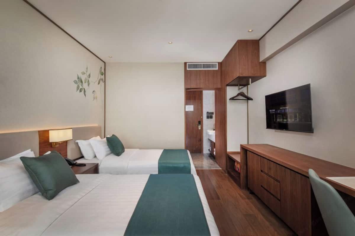 A hotel room with two beds, a desk, a TV, and a wardrobe.