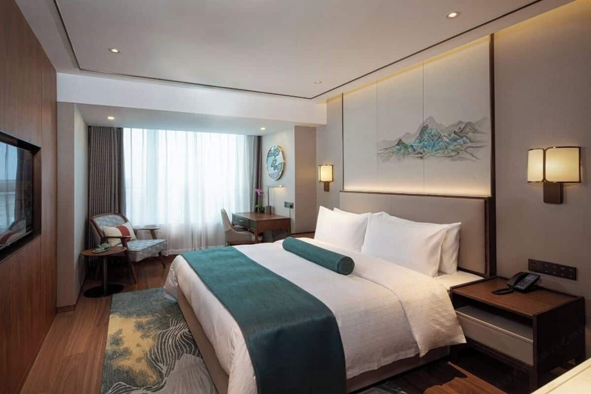 A hotel room with a bed, bedside tables, a desk, a chair, a TV, and a painting on the wall.
