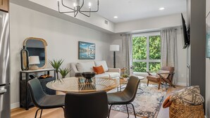 A modern living room with a dining area, a sofa set, a large window with curtains, and a television mounted on the wall. - All Year Heated Pool & Tub! New! (Bighorn No. 8)