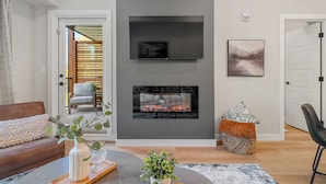 A modern living room with a fireplace, a flat-screen TV mounted above it, and a comfortable seating area with a sofa and a chair. - All Year Heated Pool & Tub! New! (Bighorn No. 8)
