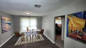 A dining area with a white table and chairs, a clock on the wall, and artwork on the walls. - Poolside Oasis (Houston)
