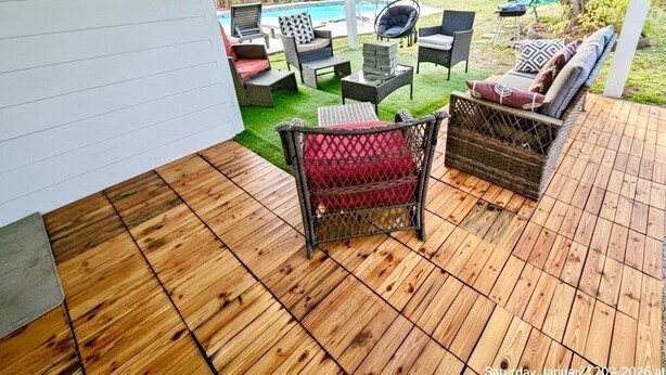 An outdoor patio with wooden flooring, wicker furniture, and a view of a backyard with a pool and a swing set. - Poolside Oasis (Houston)