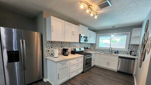 A modern kitchen with stainless steel appliances, white cabinetry, and patterned backsplash. - Poolside Oasis (Houston)
