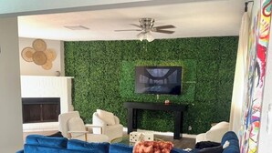 A living room with a blue sofa, a television on a black stand, and a green wall. - Poolside Oasis (Houston)