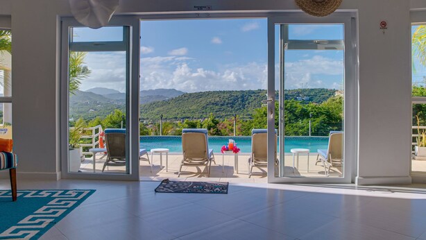 Una habitación con un amplio ventanal corredera que da a una zona de piscina con sillas de descanso y vistas a las montañas.