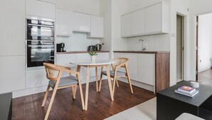 A compact kitchen with white cabinetry, a built-in oven, a coffee machine, and a small dining area with a round table and two chairs. - Blueground | Bloomsbury 1bd apartment (London)