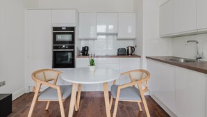 A modern kitchen with white cabinets, a round dining table, two wicker chairs, and a small potted plant. - Blueground | Bloomsbury 1bd apartment (London)