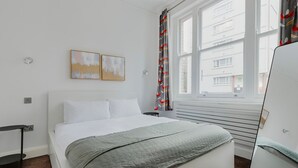 A modern bedroom with a bed, a window with curtains, and two wall-mounted paintings. - Blueground | Bloomsbury 1bd apartment (London)