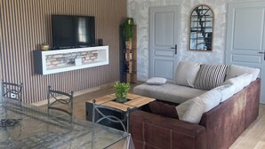 Ein modernes Wohnzimmer mit einem Glastisch, einer Couch und einem an einer Ziegelwand montierten Fernseher.