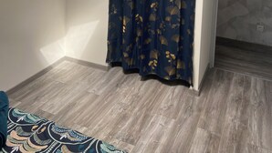 Ein Zimmer mit Oberlicht, einer Duschvorhang mit Blätermotiv, einem Wand-Fernseher und einem gemusterten Teppich.