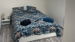 Ein Schlafzimmer mit Dachfenster, einem Bett mit gemusterten Betttextilien, einem Nachttisch mit Lampe und Holzboden.