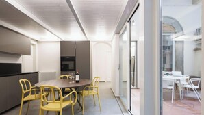 A modern kitchen with a dining area, featuring a round table and yellow chairs, and a view through a glass door to an outdoor patio.