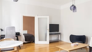 A modern, well-lit room with a bed, a desk, a chair, a television, and a dining table. - Blueground | Mariahilf, fully furnished & ready (Vienna)