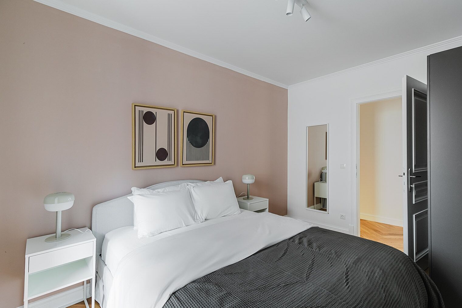 A bedroom with a bed, bedside tables, a mirror, and two framed artworks on the wall.