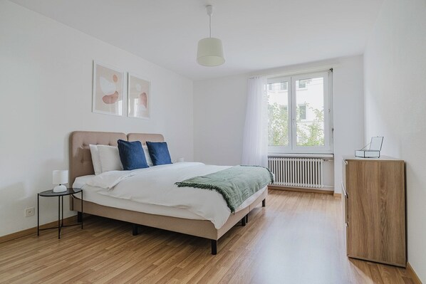 Une chambre à coucher comprenant un lit, une table de chevet, un radiateur, une fenêtre avec des rideaux et une armoire en bois.