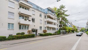 Ein mehrstöckiges Wohngebäude mit Balkonen, einer Bushaltestelle und einer freien Straße.
