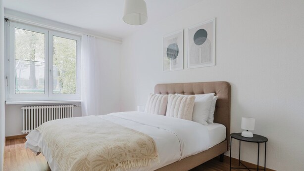 Ein Schlafzimmer mit einem Bett, einem Heizkörper, einem Fenster und zwei gerahmten Kunstwerken an der Wand.
