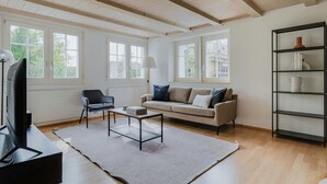 A living room with a sofa, armchair, coffee table, TV, and bookshelf. - Blueground | Fluntern, private w/d, walk to market (Zurich)