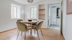 A modern dining area with a round table and four chairs, a pendant light, and a view of the kitchen through an open door. - Blueground | Fluntern, private w/d, walk to market (Zurich)