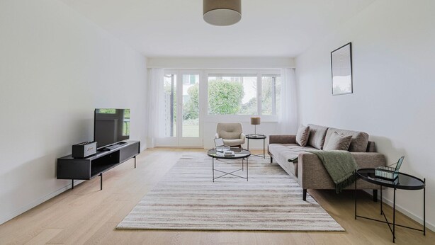 A modern living room with a sofa, a coffee table, a TV stand, and a large window.
