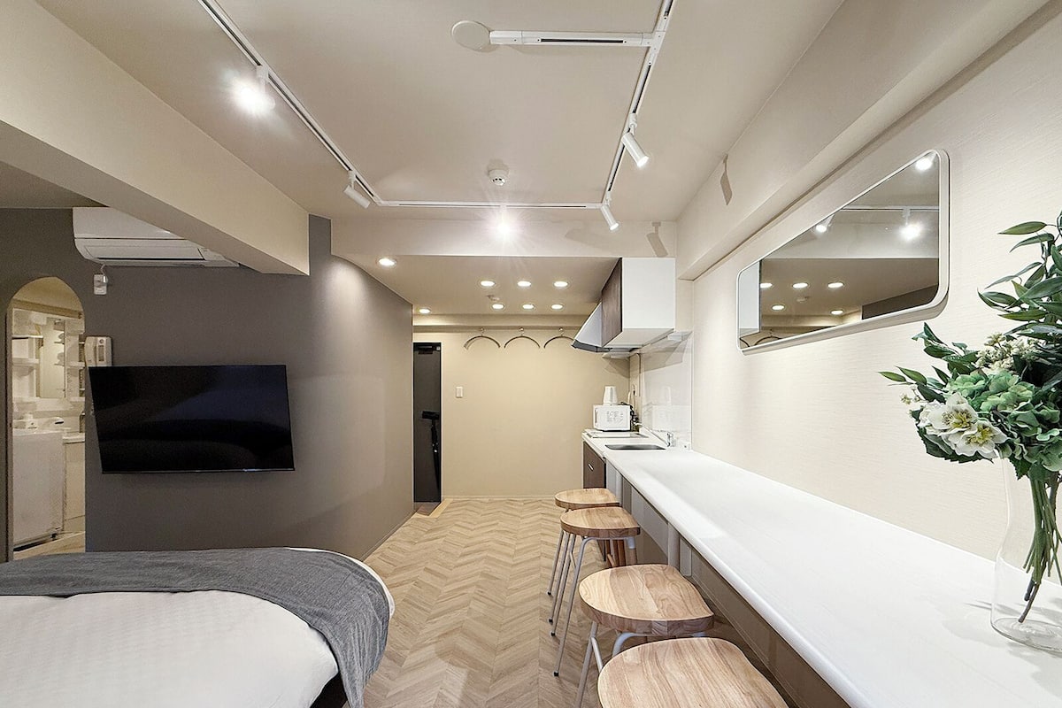 A modern hotel room with a bed, a TV, a kitchenette, and a bathroom.
