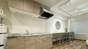 A modern kitchen with wooden cabinets, a built-in stove, and a dining area with a round mirror and chairs. - Clio Matoba by b-hotel (Hiroshima)