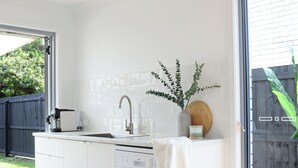 Una cocina moderna con armarios blancos, lavavajillas y un fregadero. Hay una lámpara de techo de madera y una planta en maceta sobre la encimera.