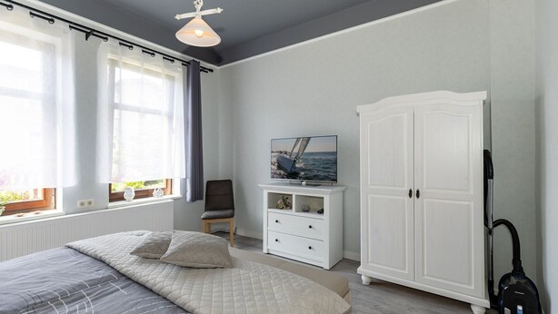 Ein Schlafzimmer mit einem Bett, einem Fernseher auf einer Kommode, einem Kleiderschrank und einem Staubsauger.
