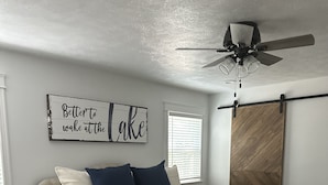 A bedroom with a bed, a ceiling fan, a wooden chest of drawers, a rug, and a wall sign.
