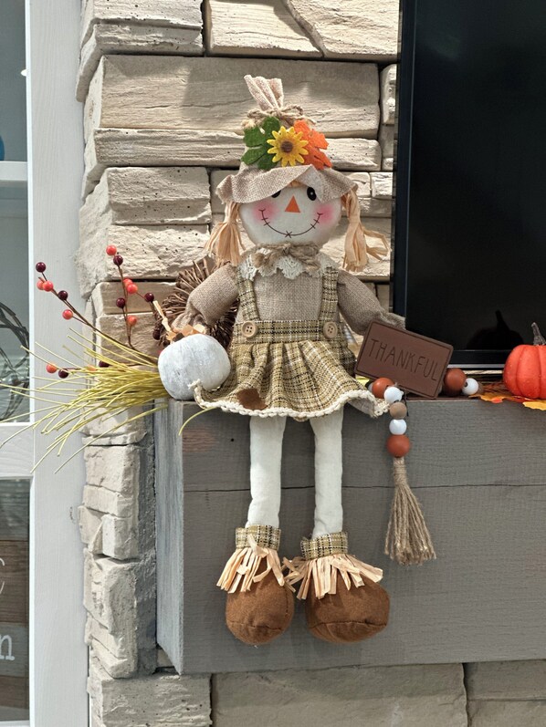 A decorative scarecrow with a 'THANKFUL' sign, placed on a wooden ledge against a stone wall.
