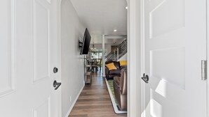 Un pasillo con una escalera que conduce a una sala de estar, un televisor de pantalla plana montado en la pared y un sofá de cuero marrón con un cojín amarillo.