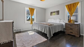 Un dormitorio con cama, mesita de noche y ventana con cortinas.