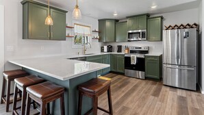 Una cocina moderna con armarios verdes, electrodomésticos de acero inoxidable y una isla central con taburetes.