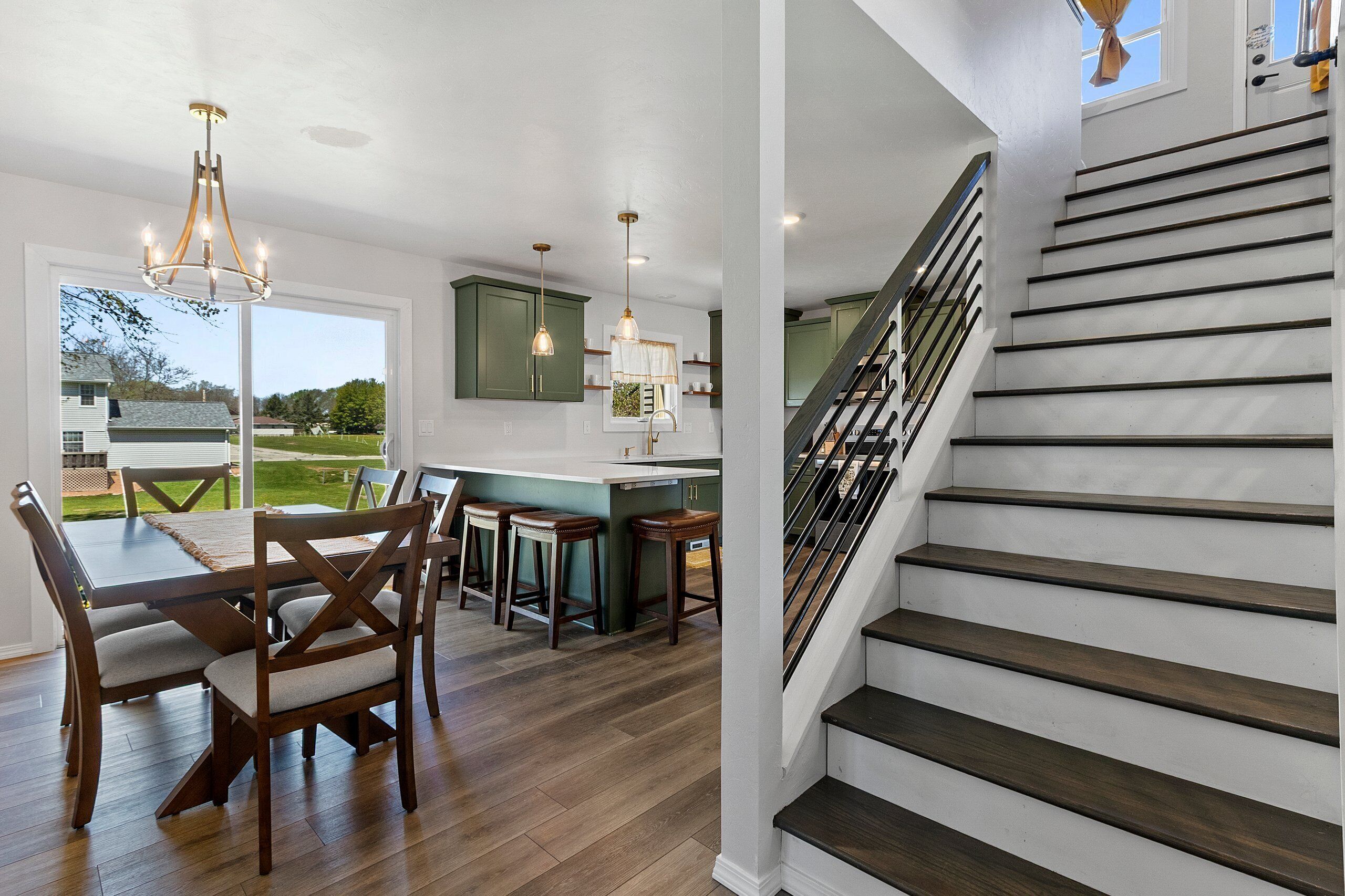A modern kitchen with a central island, wooden flooring, and a staircase with dark steps leading to an upper level.