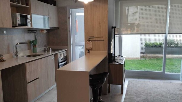 A modern kitchen with a central island, built-in appliances, and a large sliding glass door leading to a balcony. - Beautiful and comfortable department (Ñuñoa)