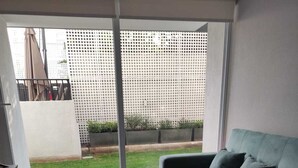 A living room with a grey sofa, a large window, and a view of a garden. - Beautiful and comfortable department (Ñuñoa)