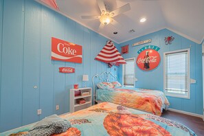 A bedroom with two beds, a ceiling fan, and Coca-Cola themed decorations.